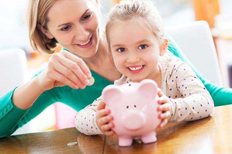 Parent and child putting money into a piggy bank and smiling, Teaching kids about money
